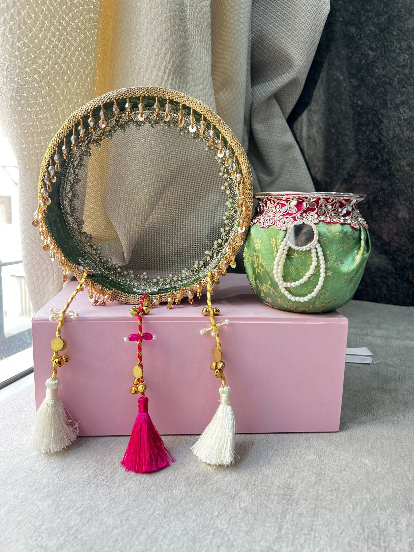 Green Karwa Chauth chalni with pink and cream tassels beside the decorated karwa